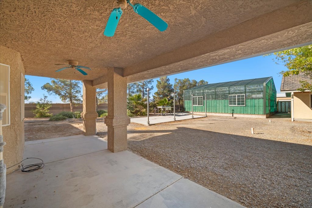 View from covered patio showing outdoor kitchen slab and commercial greenhouse